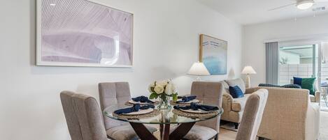 A dining area with a glass table surrounded by chairs, a vase with flowers, and artwork on the walls.