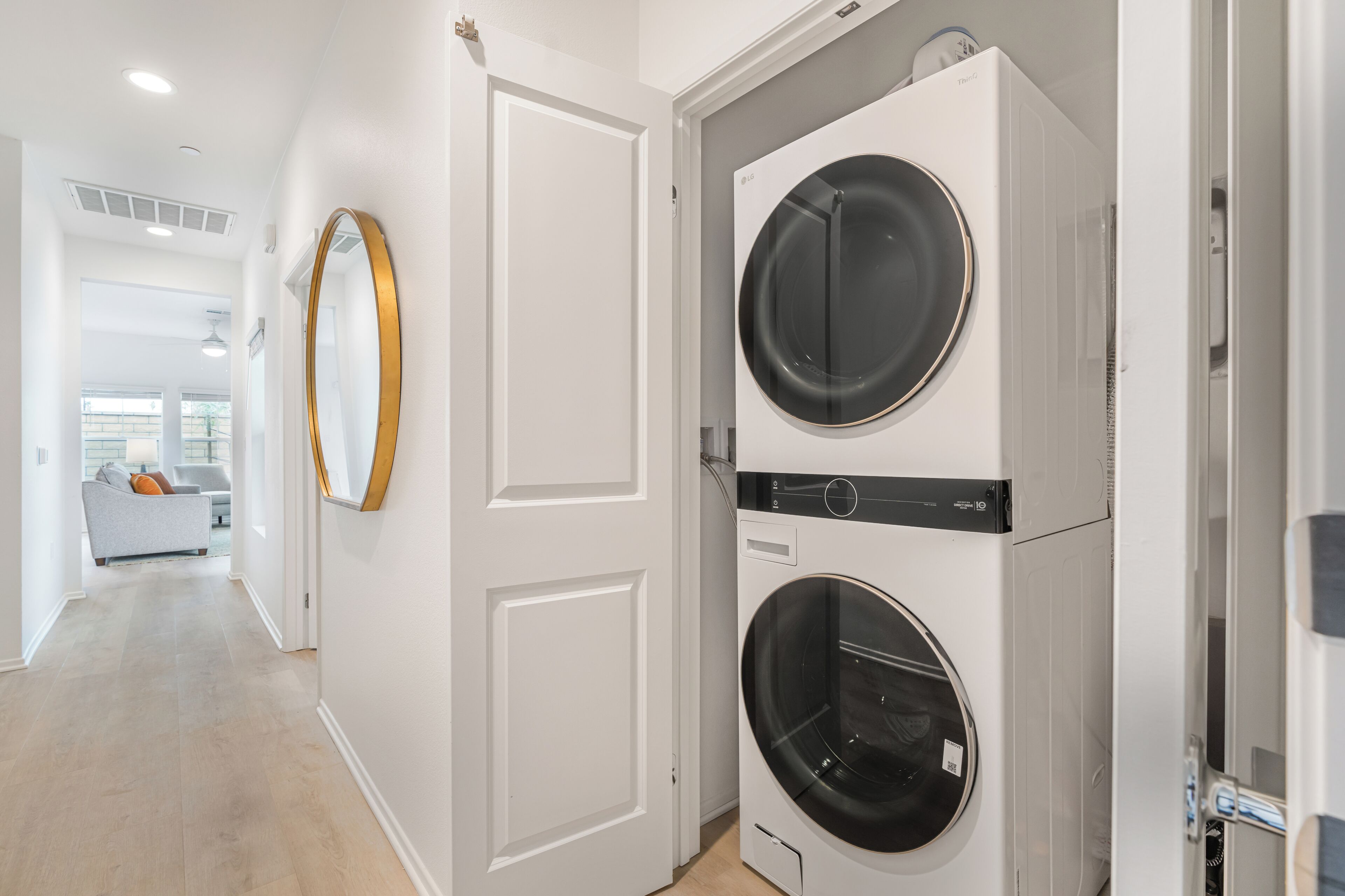 A laundry room with two stacked front-loading washing machines, a door, and a hallway leading to a living area.