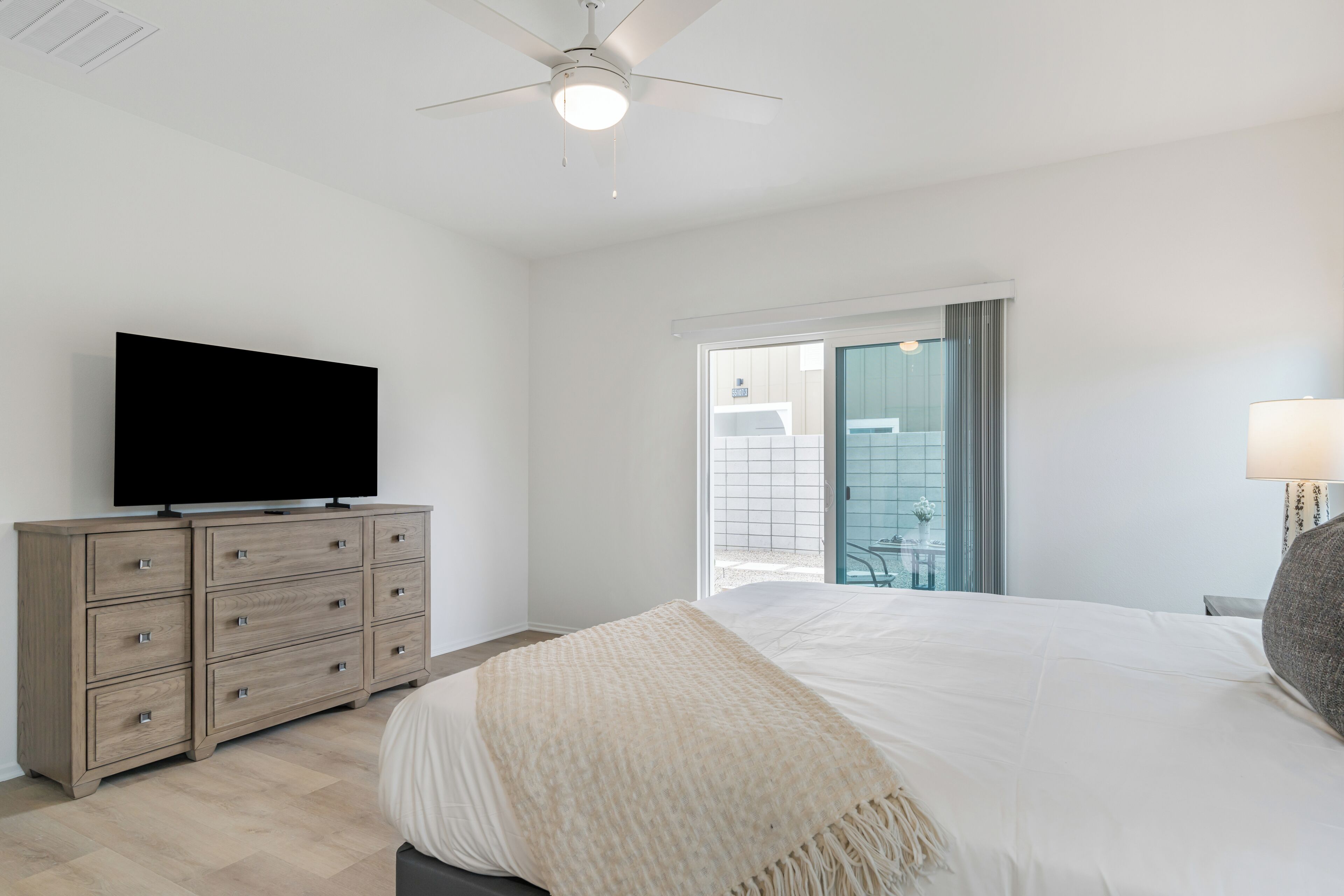 Una camera da letto con un letto, una TV su una cassettiera in legno, una ventola a soffitto e una finestra con vista.