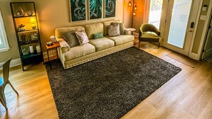 Ein Wohnzimmer mit einem beigefarbenen Sofa, einem dunklen Teppich, Holzböden und Wandbildern.