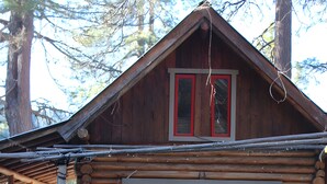 A rustic log cabin with a porch, a small window with red trim, and a wooden staircase leading to the entrance.