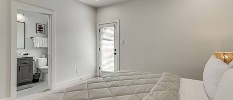 A bedroom with a large bed, a door leading to a bathroom, and a small cabinet.