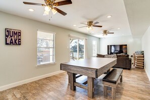 Un vaste espace de vie doté d’une grande table en bois, de plusieurs ventilateurs de plafond et d’un téléviseur.