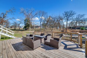 Une terrasse en bois, meublée de meubles en osier, avec un escalier et une vue sur un parc arboré et bordé de maisons.