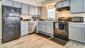 Une cuisine moderne avec des meubles gris, un réfrigérateur en acier inoxydable, un lave-vaisselle, une cuisinière et un grille-pain.