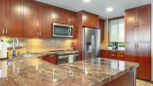 Una cocina con armarios de madera, un refrigerador de acero inoxidable, un microondas y una encimera de granito.