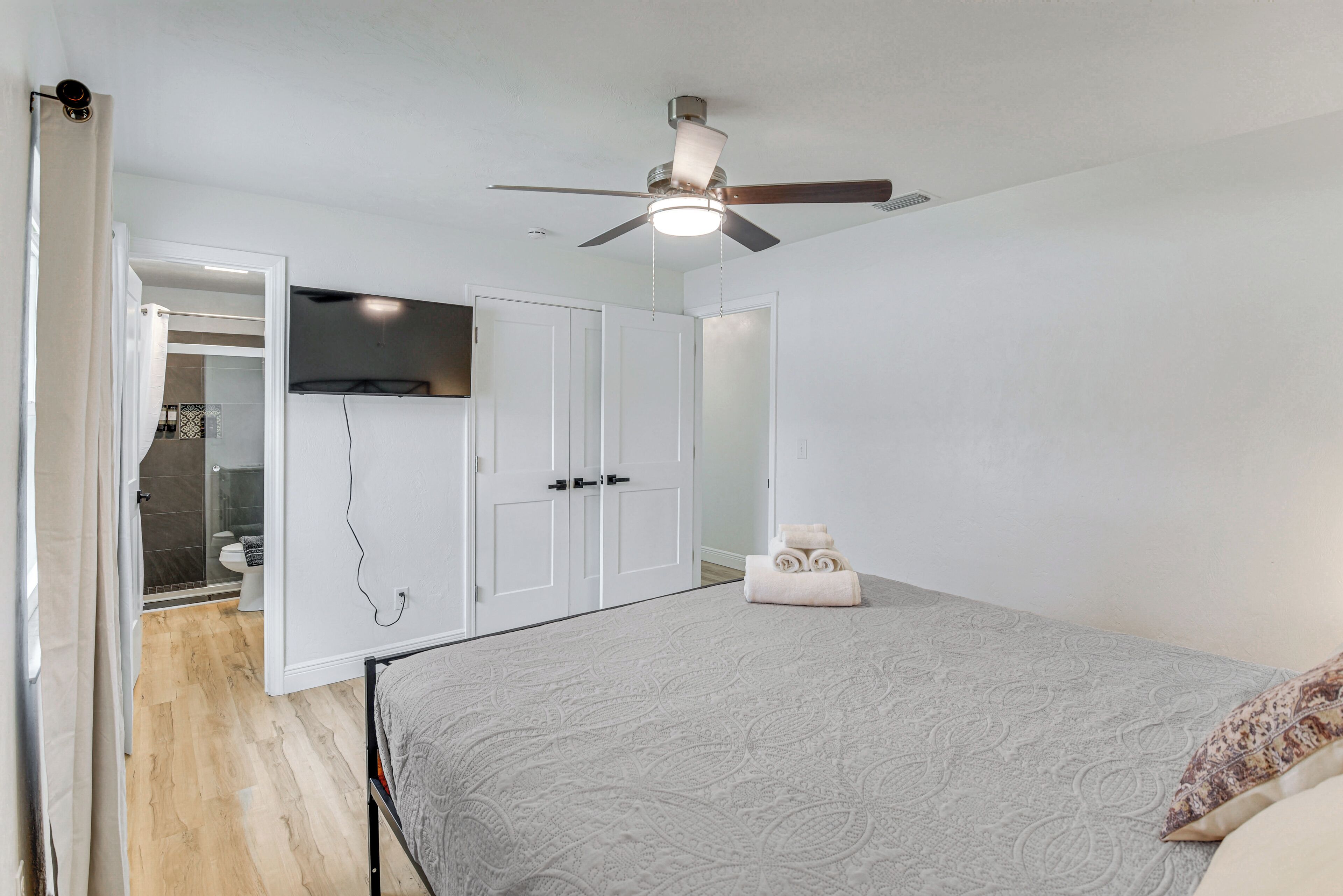A bedroom with a bed, a ceiling fan, a wardrobe, and a bathroom visible through an open door.