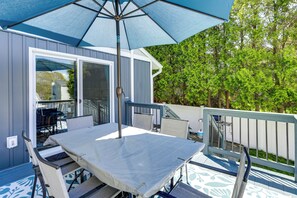 Une terrasse couverte avec une table et des chaises, un parasol bleu et une vue sur une maison et des arbres.