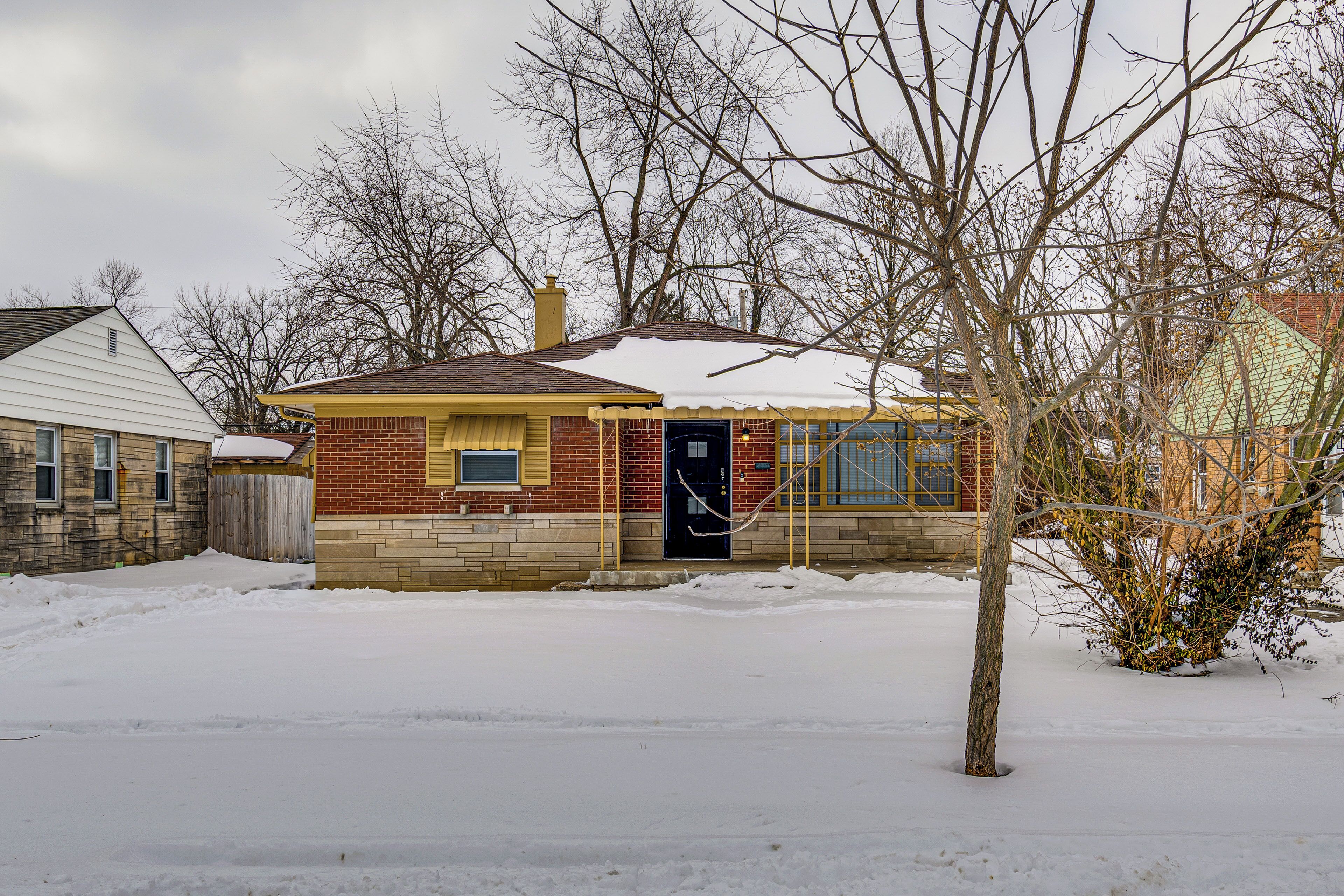 A single-story house with a brick facade, a visible front door, and a snow-covered roof.