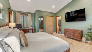 Un dormitorio con una cama grande, un televisor montado en la pared, un tocador y una ventana con cortinas.