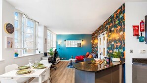 Una cocina moderna con una isla central, un comedor con sillas blancas y una pared azul decorativa.