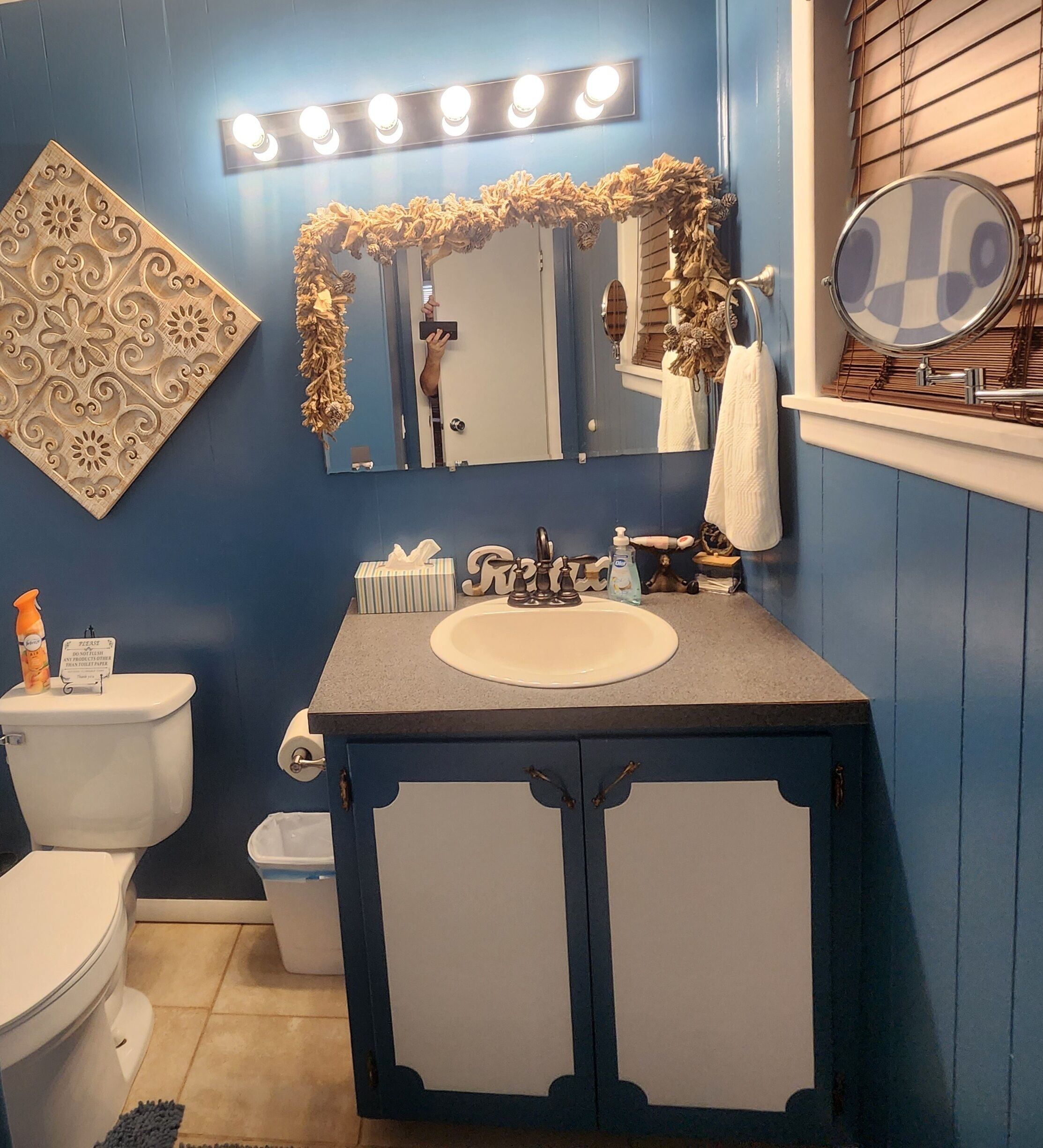 A bathroom with a blue wall, a vanity with a sink, a mirror, and a toilet.