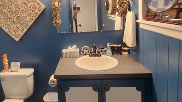 A bathroom with a blue wall, a vanity with a sink, a mirror, and a toilet.