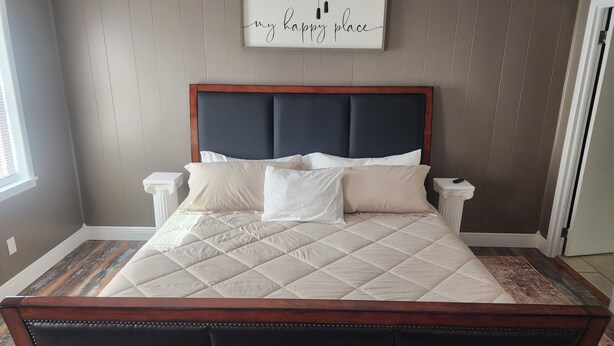 Une chambre avec un grand lit, une tête de lit sombre et un panneau décoratif sur le mur portant l’inscription « mon endroit préféré ».
