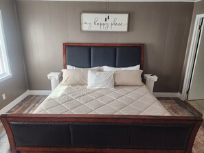 Un dormitorio con una cama grande, un cabecero oscuro y un letrero en la pared que dice 'mi lugar feliz'.