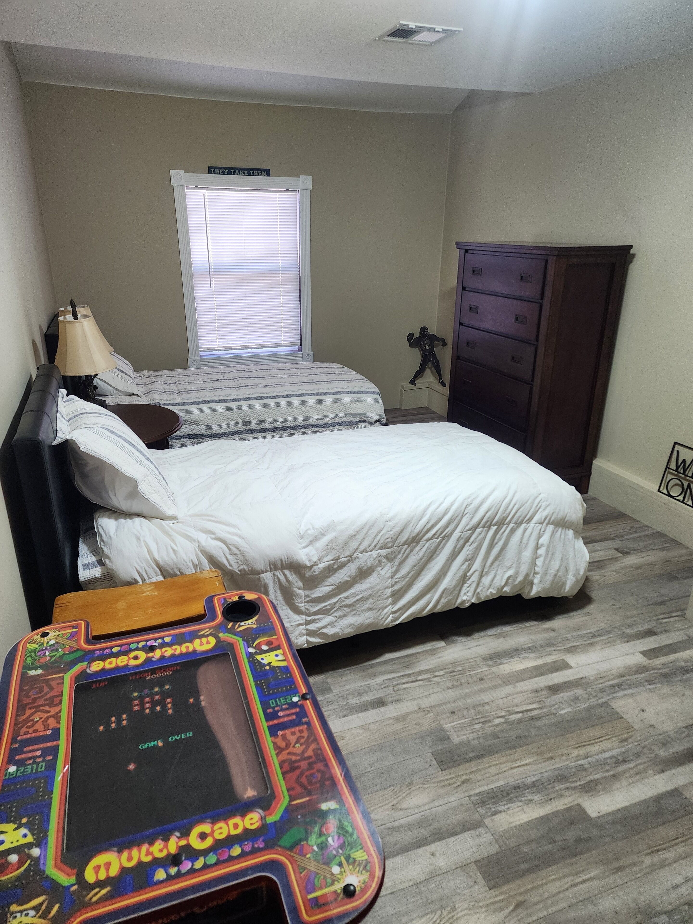 A bedroom with two beds, a dresser, a lamp, and a Nintendo Switch console.