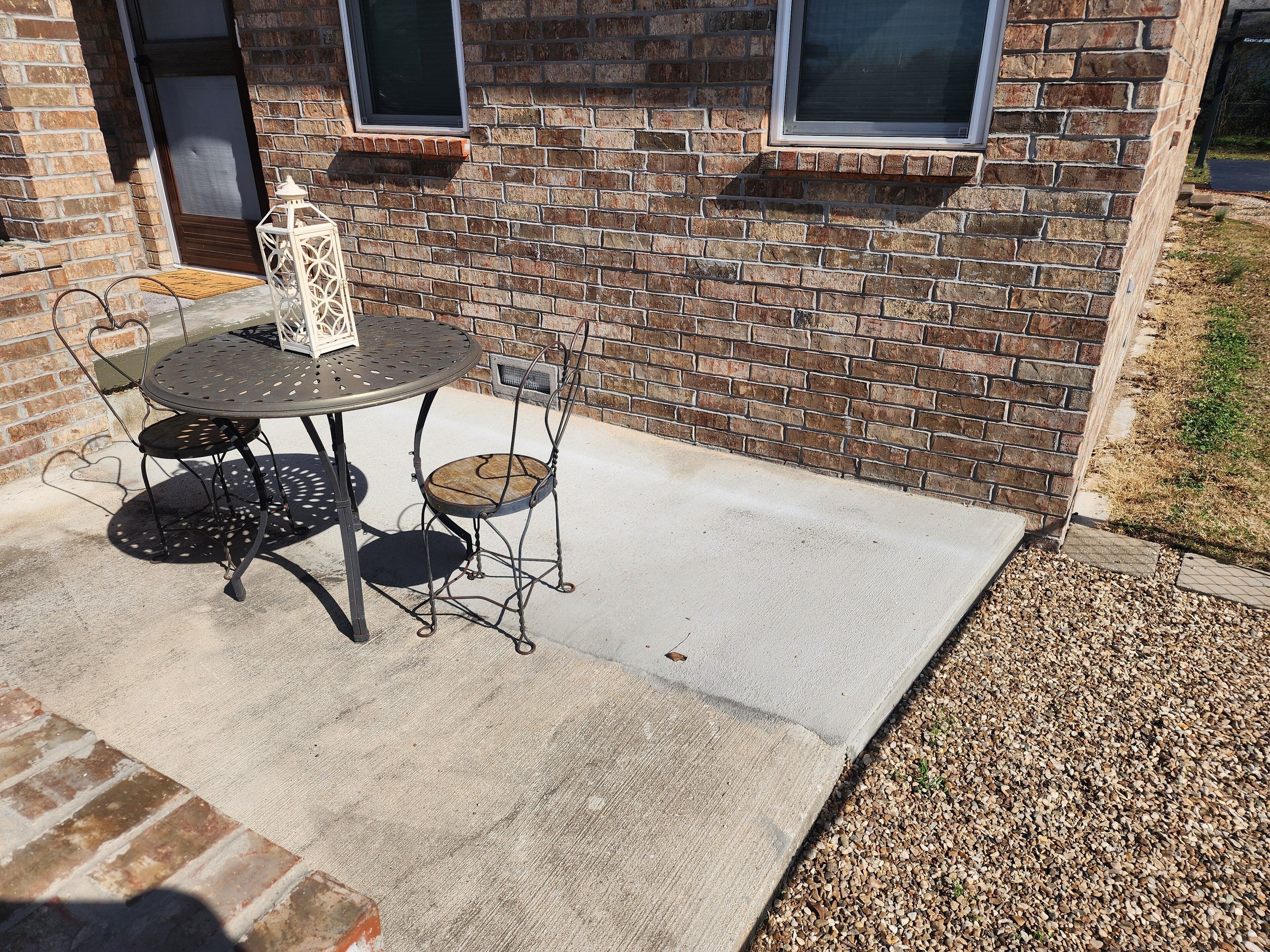 A patio with a round metal table and chairs, a lantern, and a brick wall with windows.