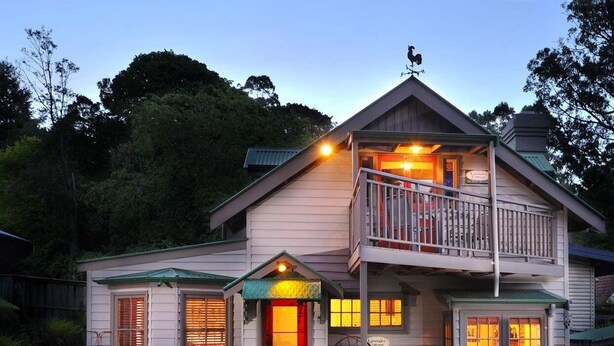 A two-story house with a balcony, a red door, and a well-maintained garden.