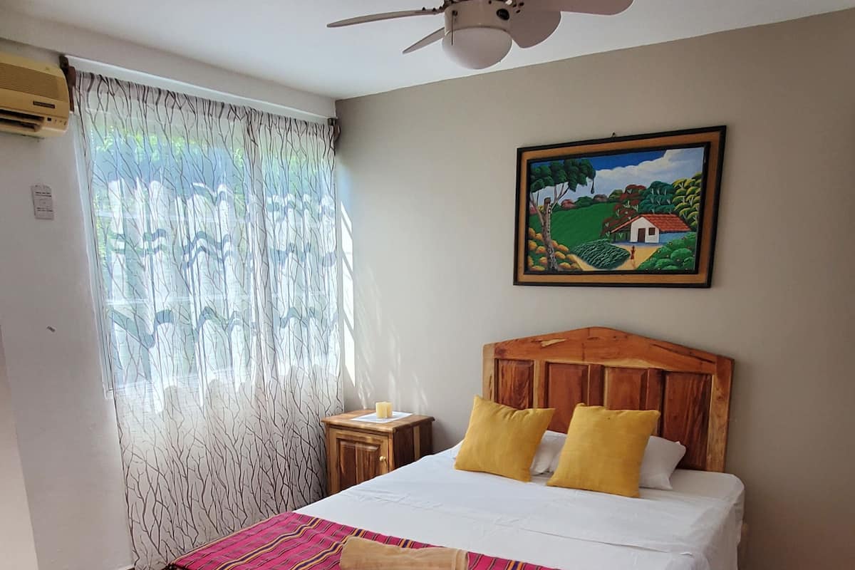 Un dormitorio con cama, ventilador de techo, un cuadro y suelo estampado.