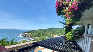 Vista a la piscina con una vista despejada del océano, un balcón con pérgola y abundante vegetación.