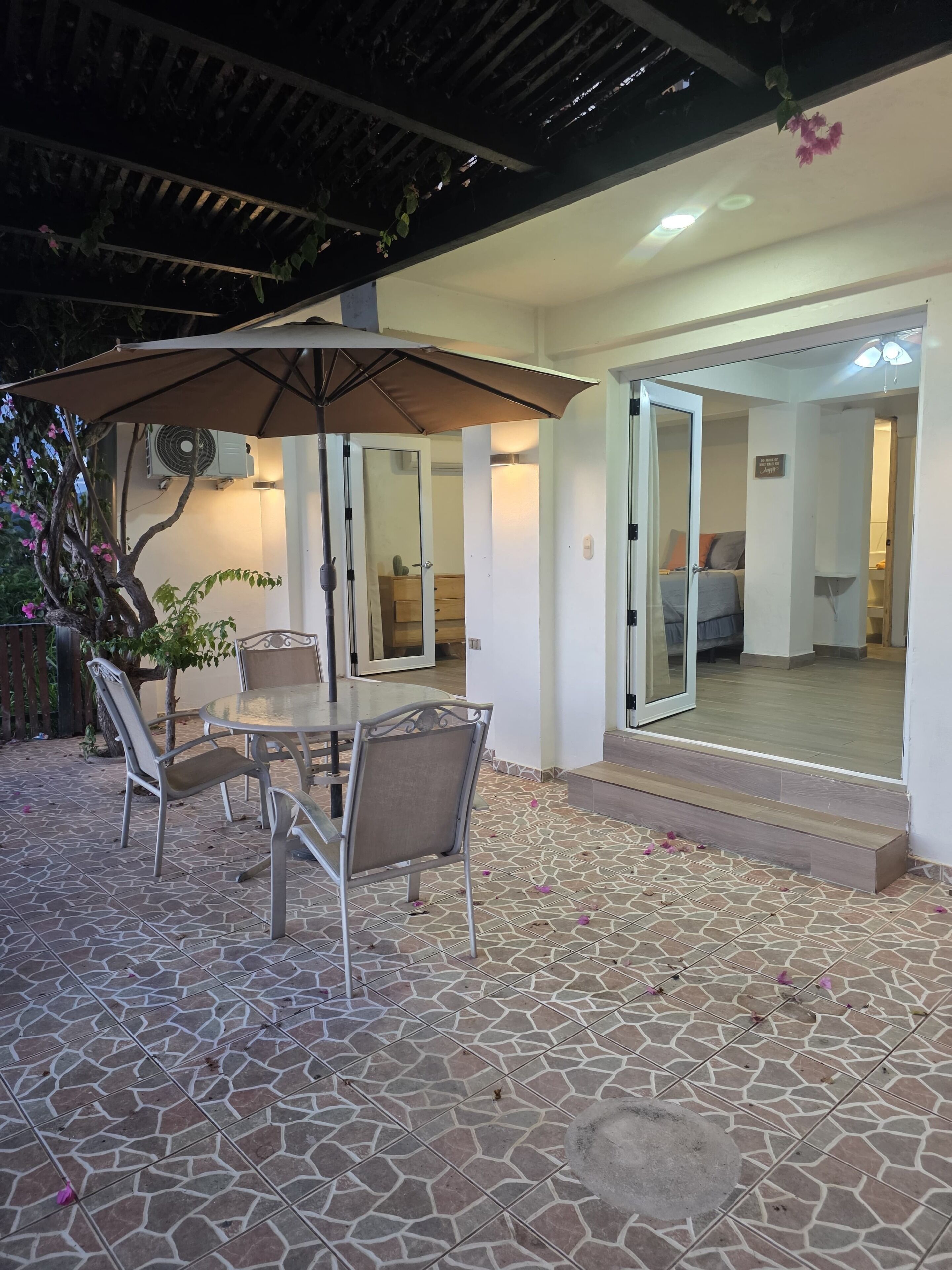 Un patio al aire libre con mesa y sillas, una sombrilla y vista hacia la casa.