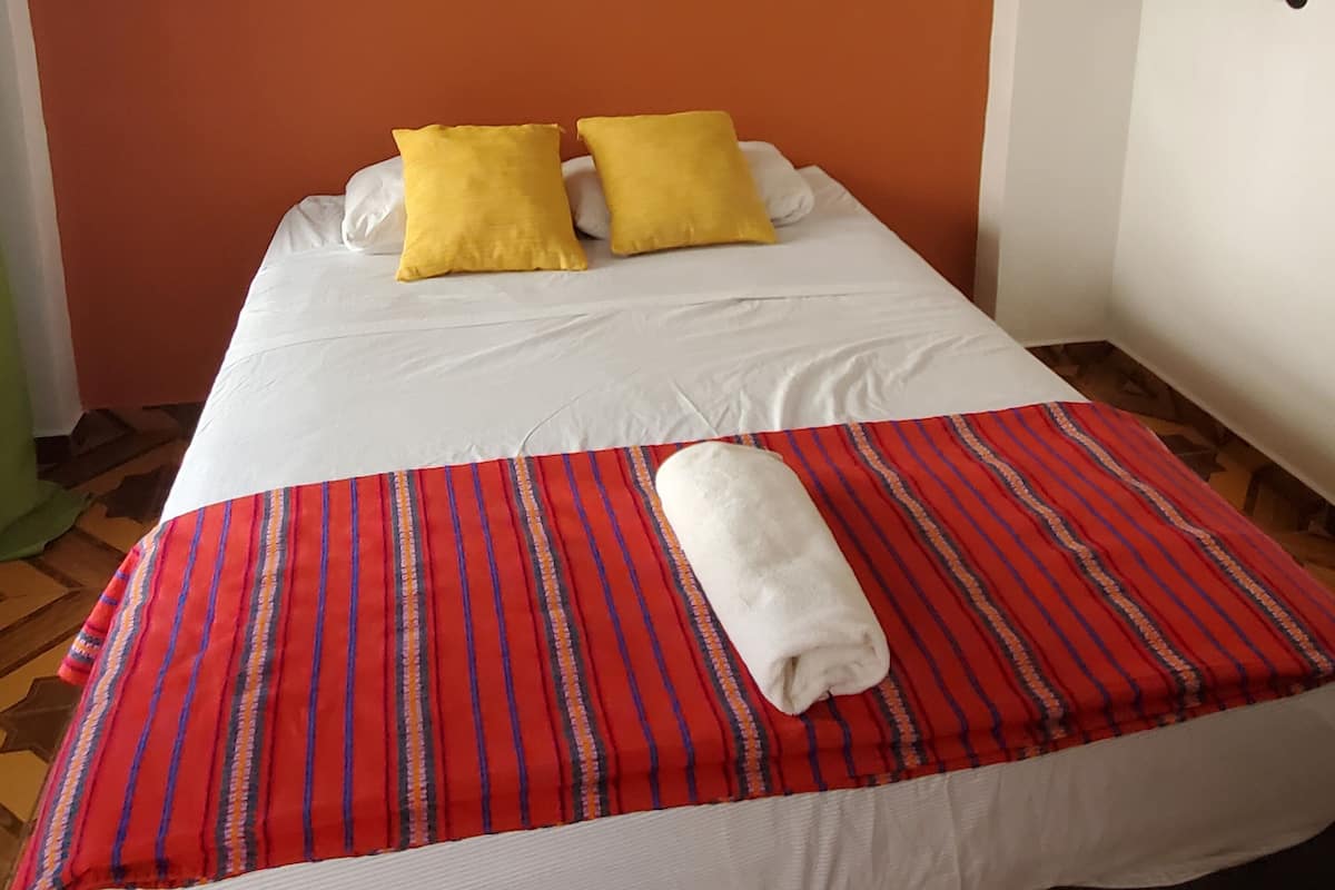 Habitación de hotel con cama, ropa de cama blanca, colcha a rayas rojas y un cuadro de cabañas de playa en la pared.