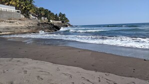 Una playa con olas, palmeras y un acantilado rocoso.