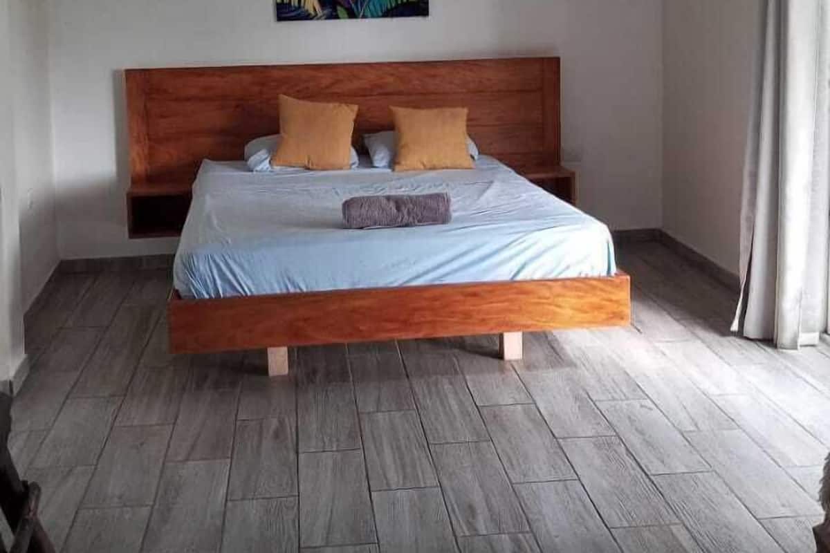 Un dormitorio con una cama de madera, un ventilador de techo y un cuadro colorido en la pared.