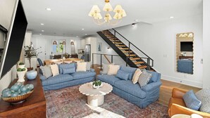 A spacious living room with a sectional sofa, a coffee table, and a staircase leading to an upper level. - 8th Ave South Gem Fabulous Home for Groups of 12 (Nashville)