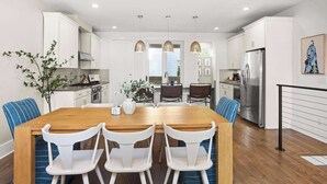A modern kitchen with white cabinets, a wooden dining table, and blue chairs. - 8th Ave South Gem Fabulous Home for Groups of 12 (Nashville)