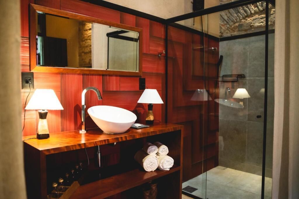 A bathroom with a wooden vanity, a large mirror, two wall-mounted lamps, a white sink, and a glass shower enclosure.