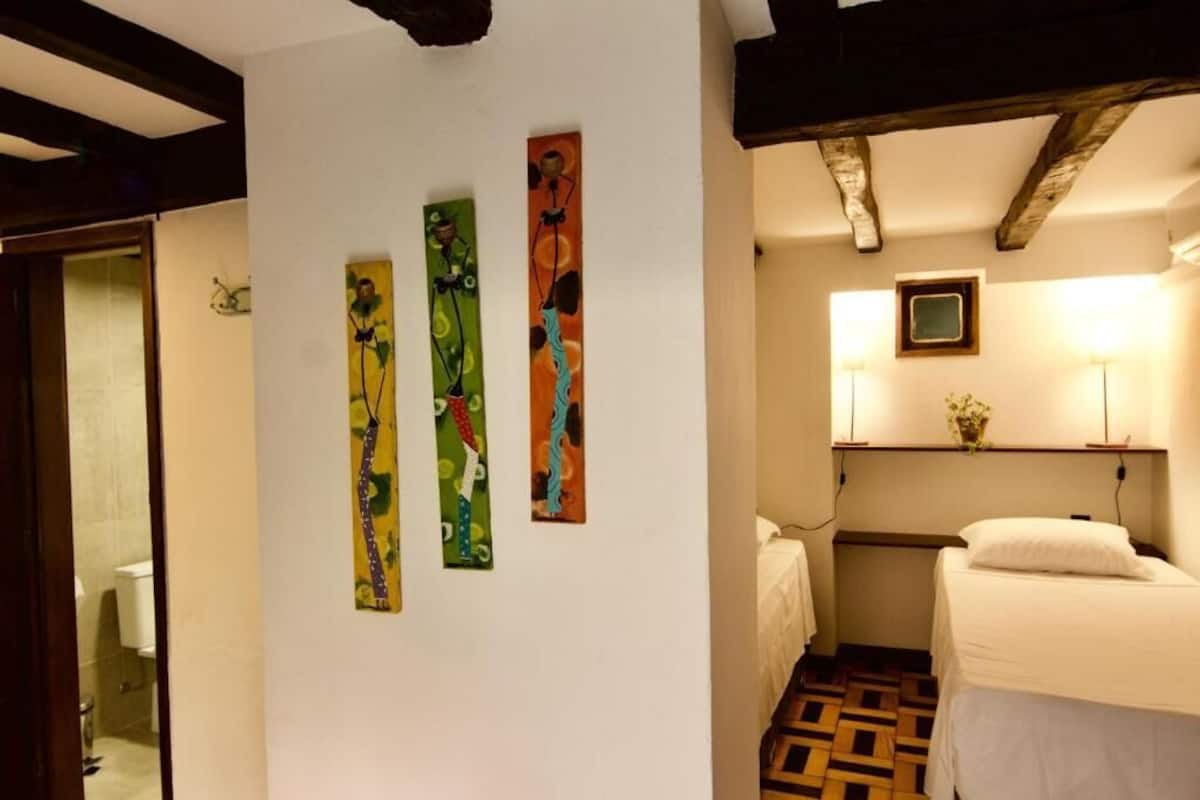 Una habitación con una cama, un estante en la pared con una planta y tres obras de arte verticales.