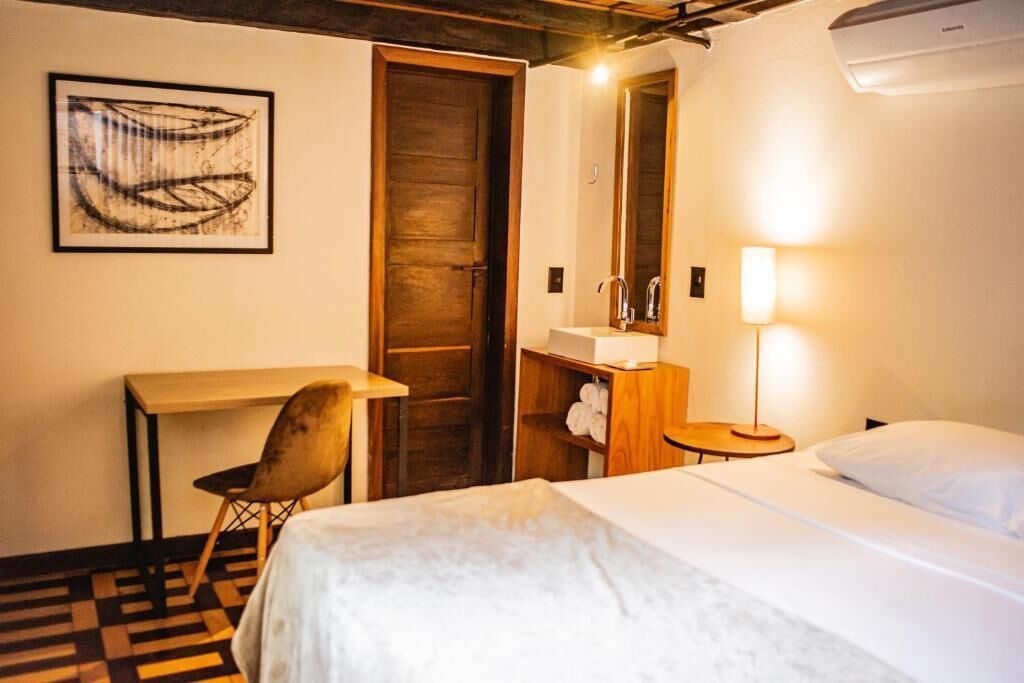 Habitación de hotel con cama, escritorio, silla, espejo, lavabo y aire acondicionado instalado en la pared.