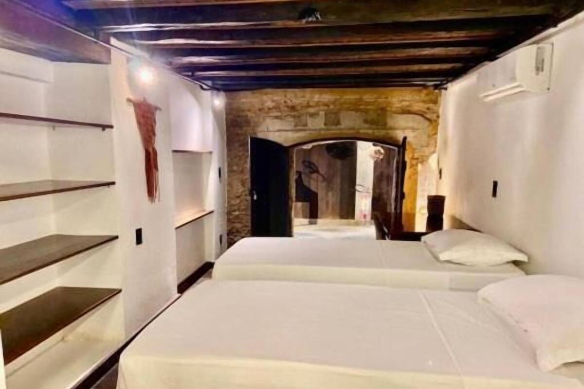 Una habitación estrecha con dos camas, una pared de piedra y techo de madera.