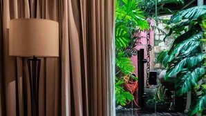 A room with a wooden table, a chair, and a lamp. There is a view of a garden with plants and a pathway leading outside. - Cas'Amazonia Brasil (Belém)