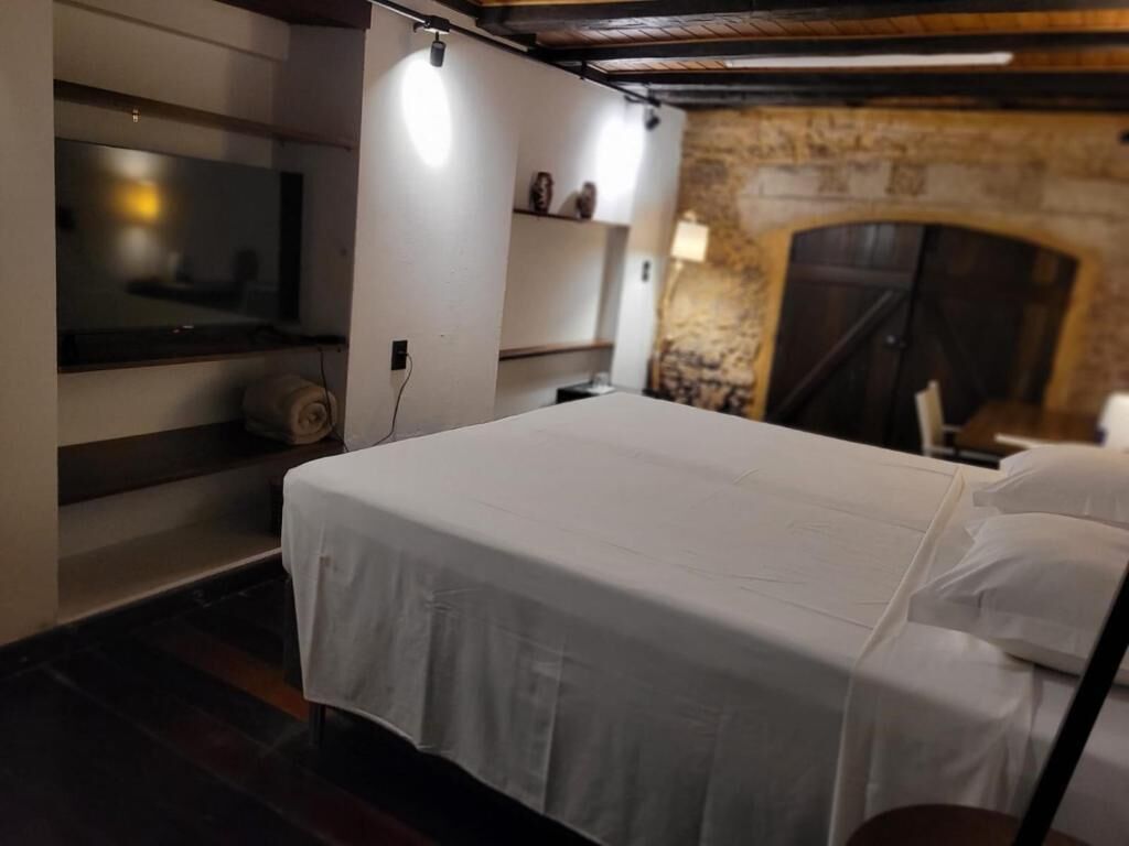 A bedroom with a bed, a television, a stone wall, and a fireplace.