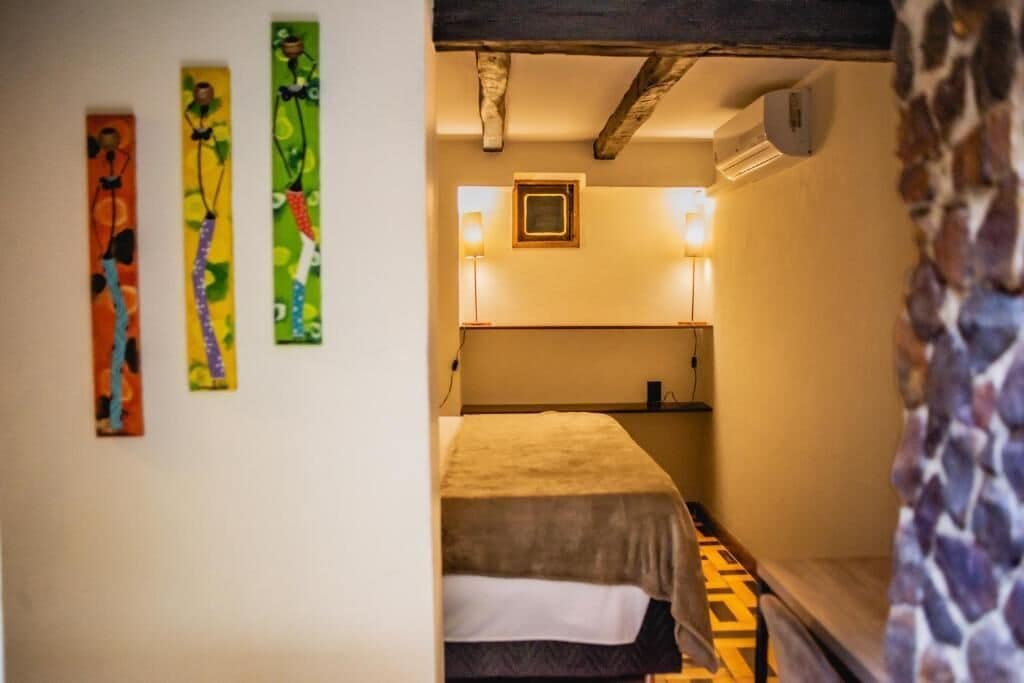 A room with a bed, a wall-mounted air conditioner, and three colorful abstract paintings.