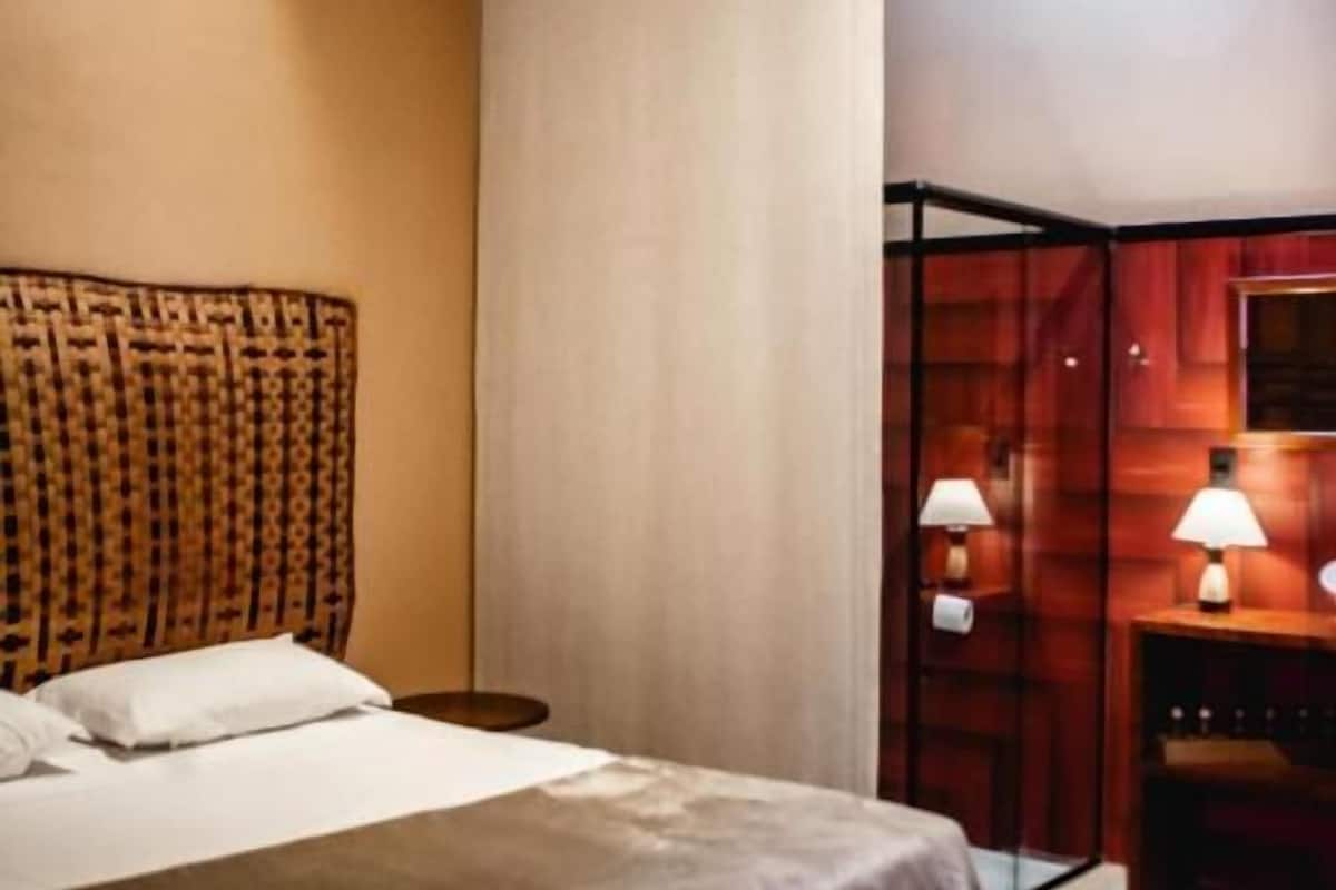 Una habitación de hotel con cama, mesita de noche y un banco de madera.