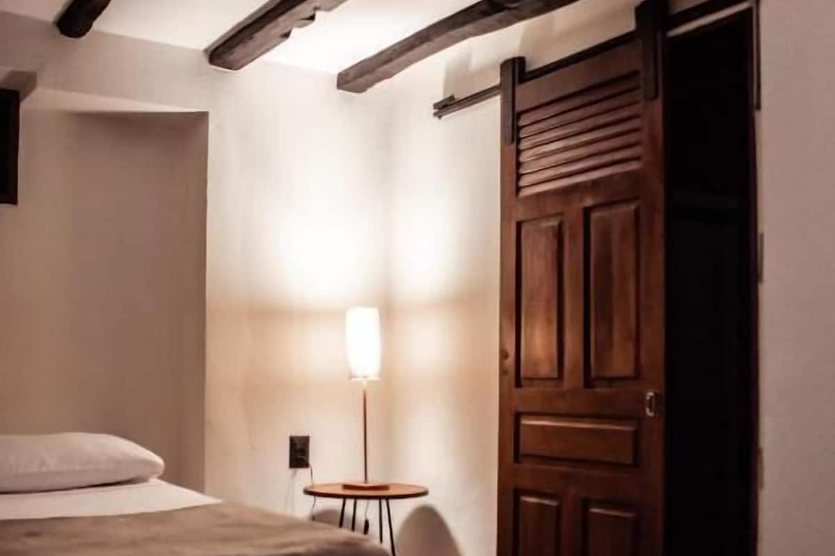 Un dormitorio con una cama, una mesita de noche, una lámpara y una puerta de madera.