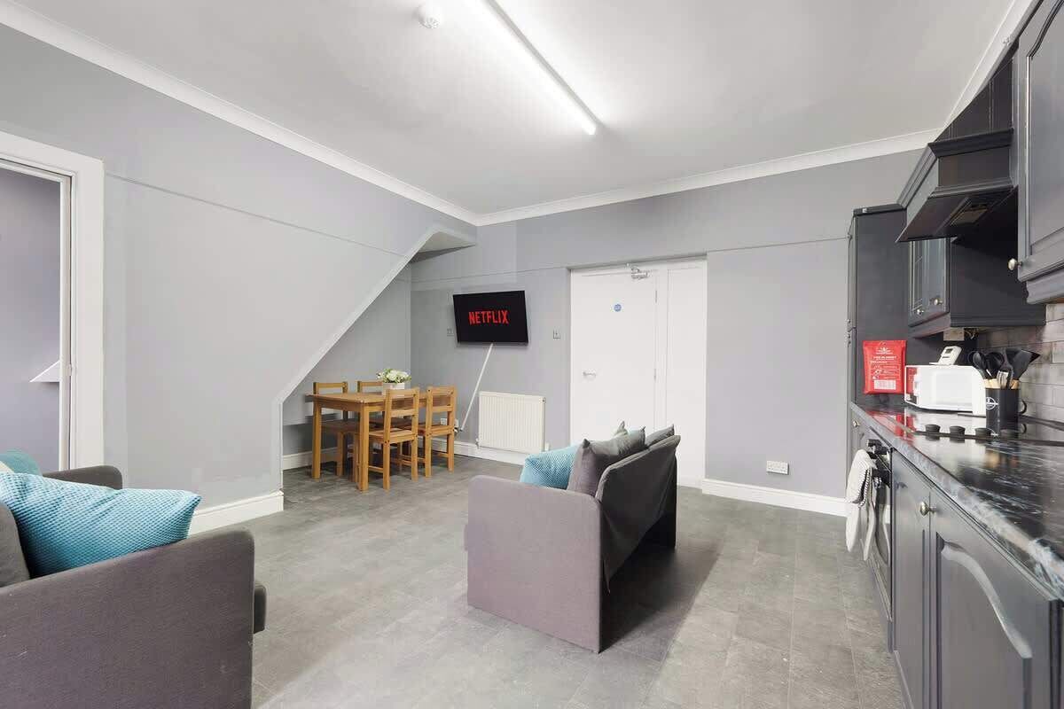 Un salon moderne comprenant un canapé, une table à manger et un coin cuisine avec des placards et un téléviseur affichant le logo « NETFLIX ».