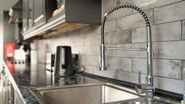 Una cocina moderna con un lavamanos de acero inoxidable, un grifo flexible y un salpicadero de azulejos.