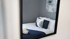 Una cama bien hecha con ropa de cama blanca y azul oscuro, una manta azul oscuro y una almohada blanca.