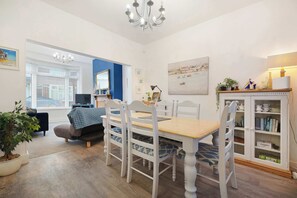 A dining area with a wooden table and white chairs, a bookshelf, a potted plant, and a painting on the wall. - Coastal 3-Bed Home for Families & Contractors (Redcar and Cleveland)