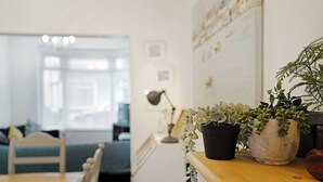 A room with a wooden table, two potted plants, a lamp, and a view of a blue sofa and chair in the background. - Coastal 3-Bed Home for Families & Contractors (Redcar and Cleveland)