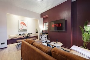 Un salon moderne avec un canapé, une table à manger, un téléviseur fixé au mur et une plante.