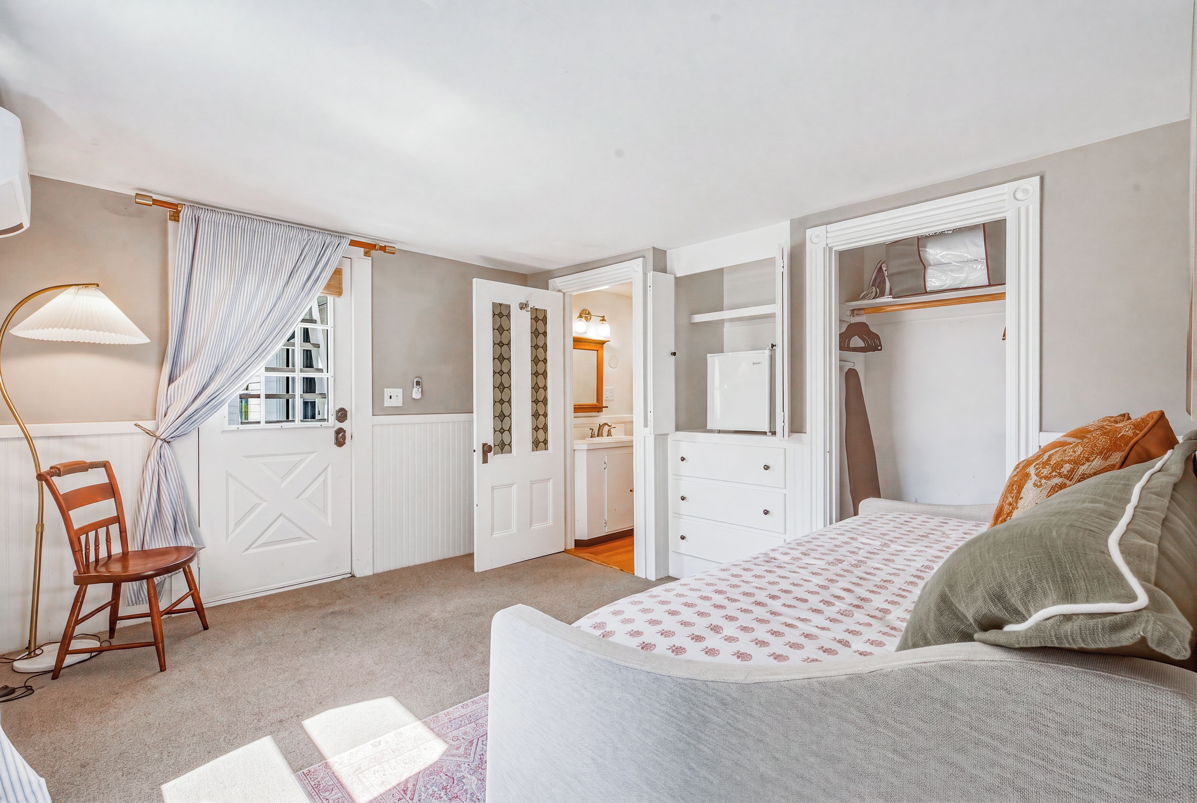 Un dormitorio con cama, una silla, un armario y un baño visible a través de una puerta abierta.