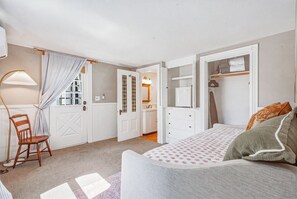 A bedroom with a bed, a chair, a wardrobe, and a bathroom visible through an open door.