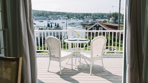 Ein Balkon mit zwei weißen Korbstühlen und einem kleinen Tisch, mit Blick auf ein Ufer mit Booten und Häusern.