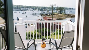 Ein Balkon mit zwei Stühlen und einem Tisch, der auf einen Hafen mit Booten und einer Mole blickt.