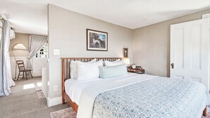 Een slaapkamer met een bed, nachtkastje, lamp, fotokader en een deur.